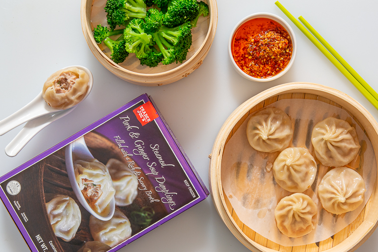 Trader Joe's Steamed Pork &amp; Ginger Soup Dumplings in a steamer basket with steamed broccoli and chili oil